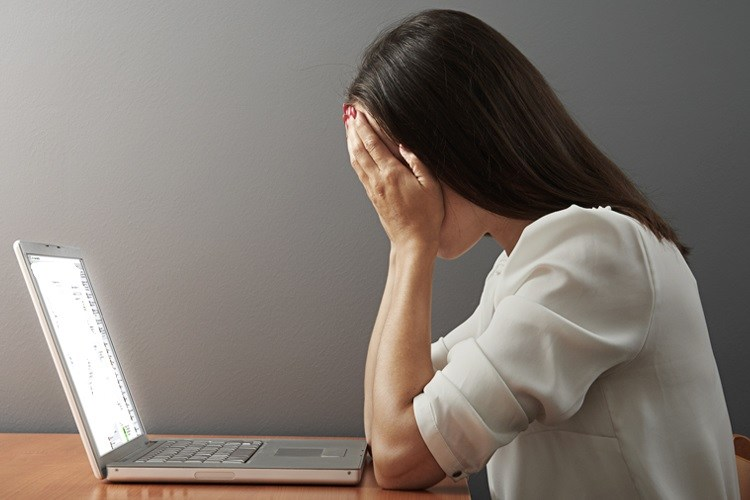 Frau sitzt vor dem Laptop mit der Handfläche im Gesicht